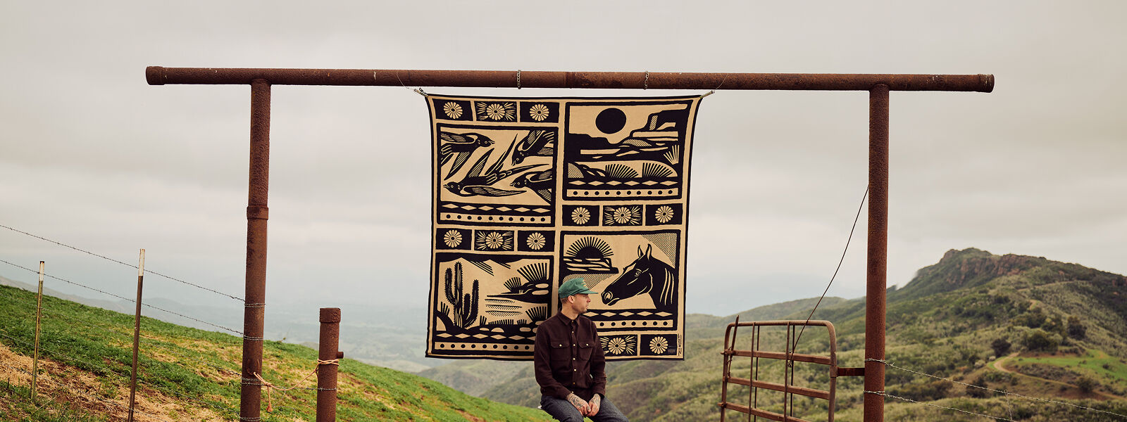 Artist Jess Mugett seated outside with his blanket design draped behind him