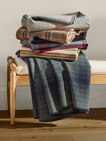 Wool blanket draped along a rope, with a cream background and warm colored patterns.