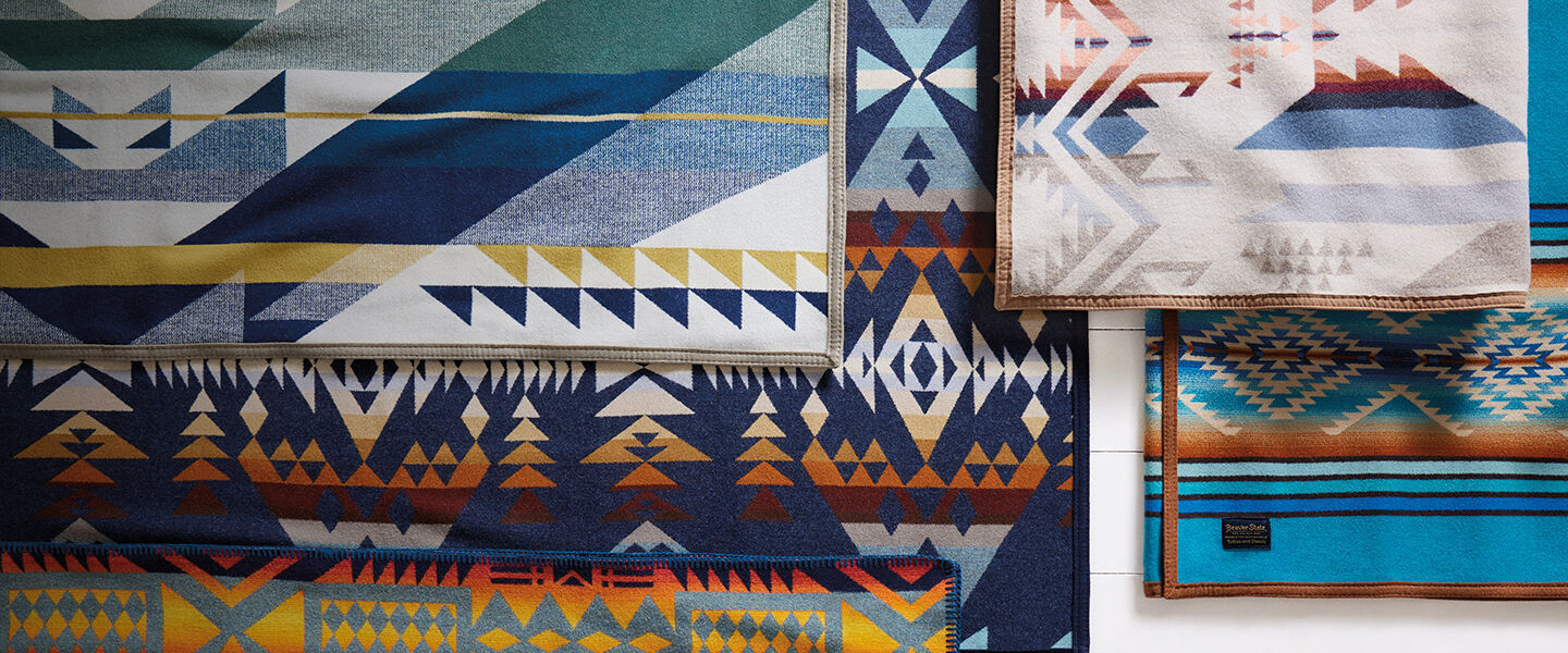 Top down view of multiple different blankets with cool toned geometric patterns woven into each of them.