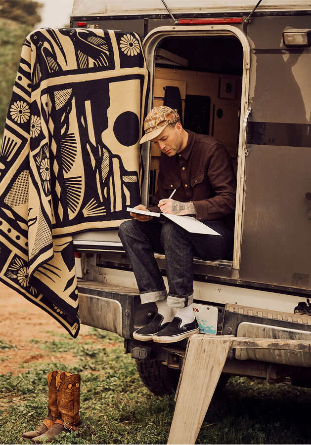 Artist Jess Mudgett sketching while seated in the back of his truck