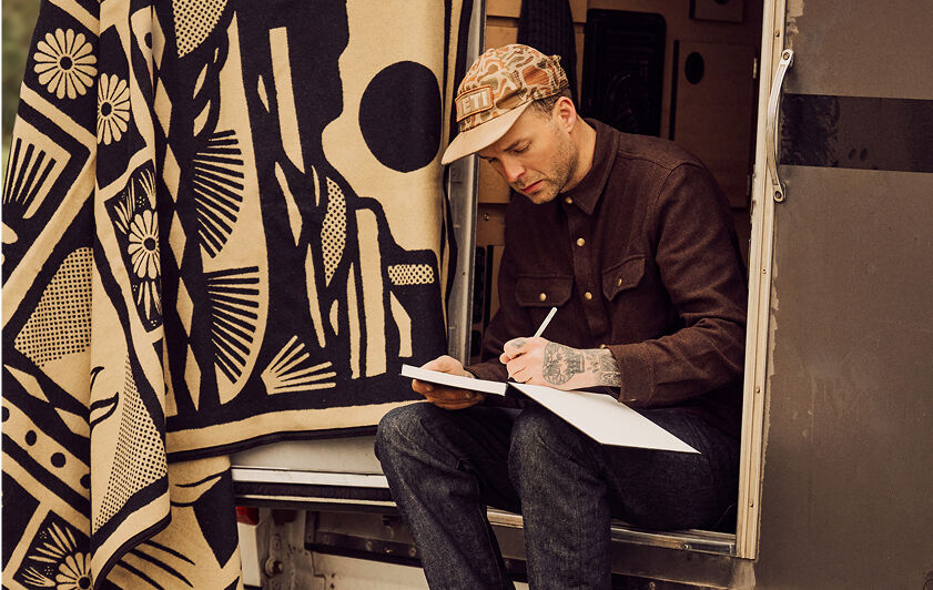 Artist Jess Mudgett sketching while seated in the bed of his truck
