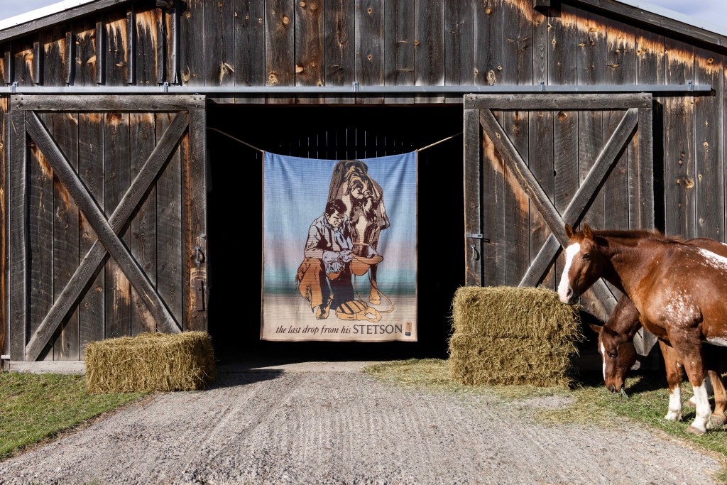 Blanket, "The Last Drop From His Stetson", hanging on the doorway of a weathered barn.