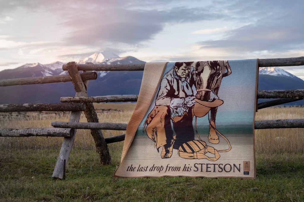 The Stetson x Pendleton blanket on a rail fence against a background of snowy mountains.