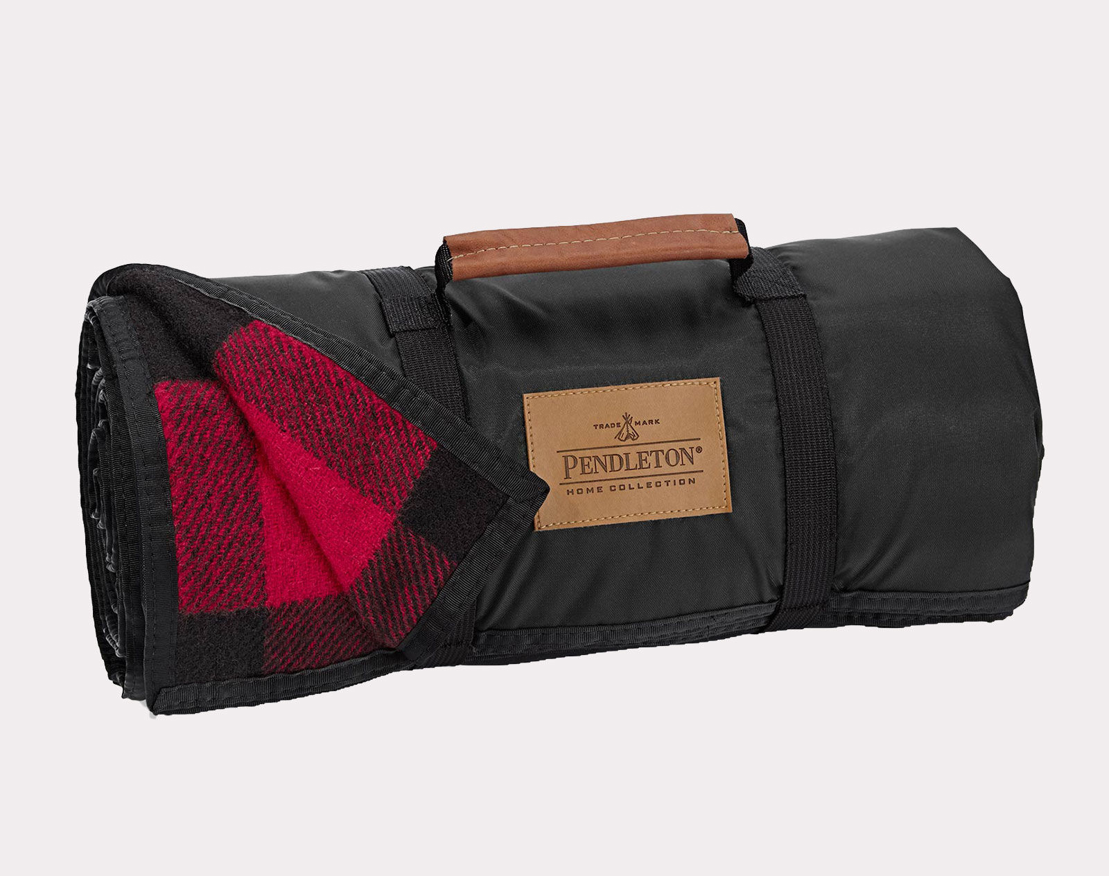 A Pendleton roll-up blanket in a black and red plaid with a black nylon backing and built-in handle with brown leather grip.