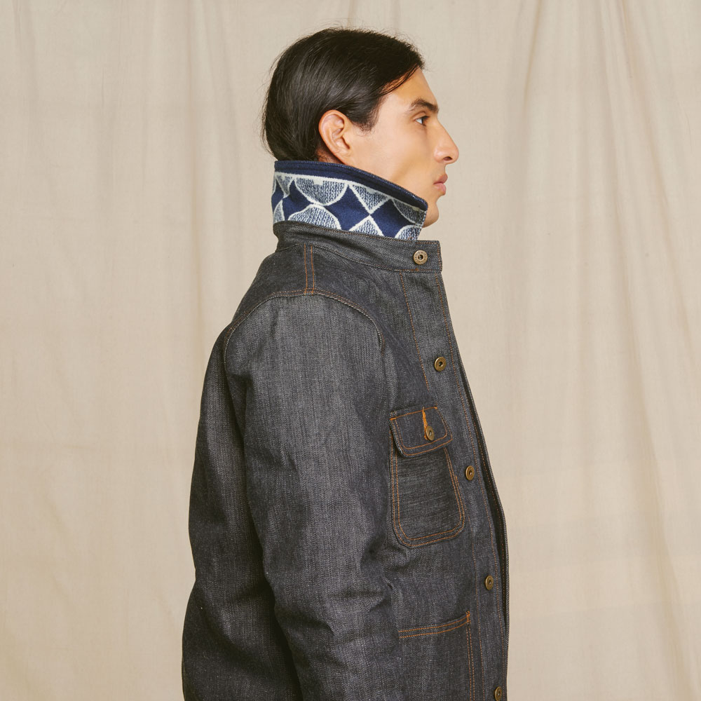 A Native American model stands in profile, wearing a Ginew jacket with the collar turned up to show that the under-collar is lined in Pendleton patterned wool.