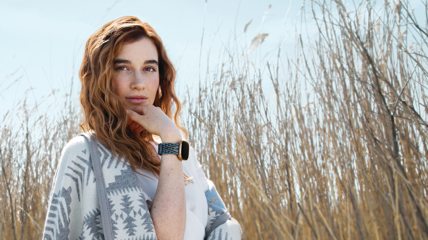 A young woman wearing a Pendleton Fitbit on her wrist and a Pendleton blanket around her shoulders
