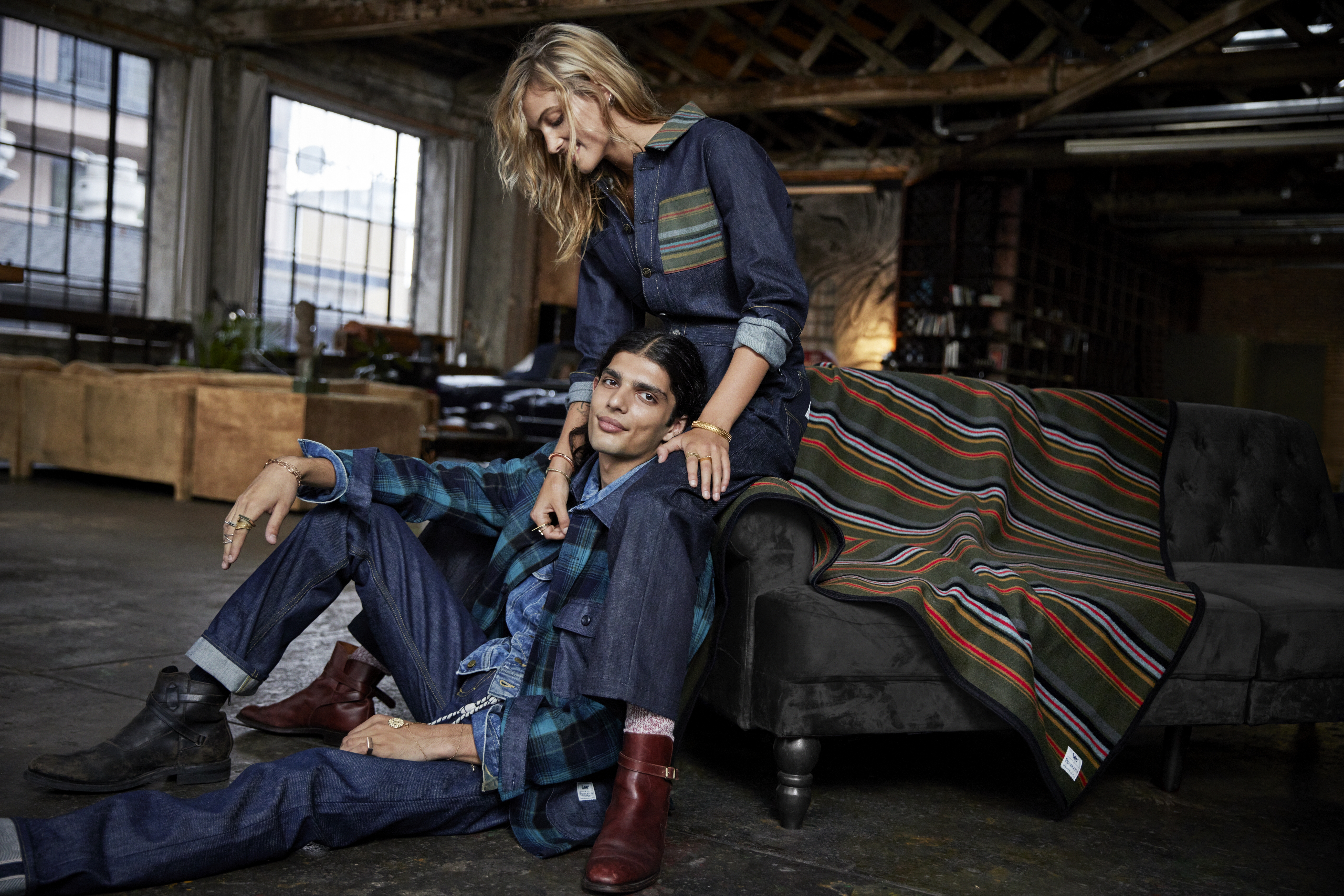 A man and woman pose wearing Cone Denim clothes from the Lee/Pendleton collaboration, with the blanket beside them.