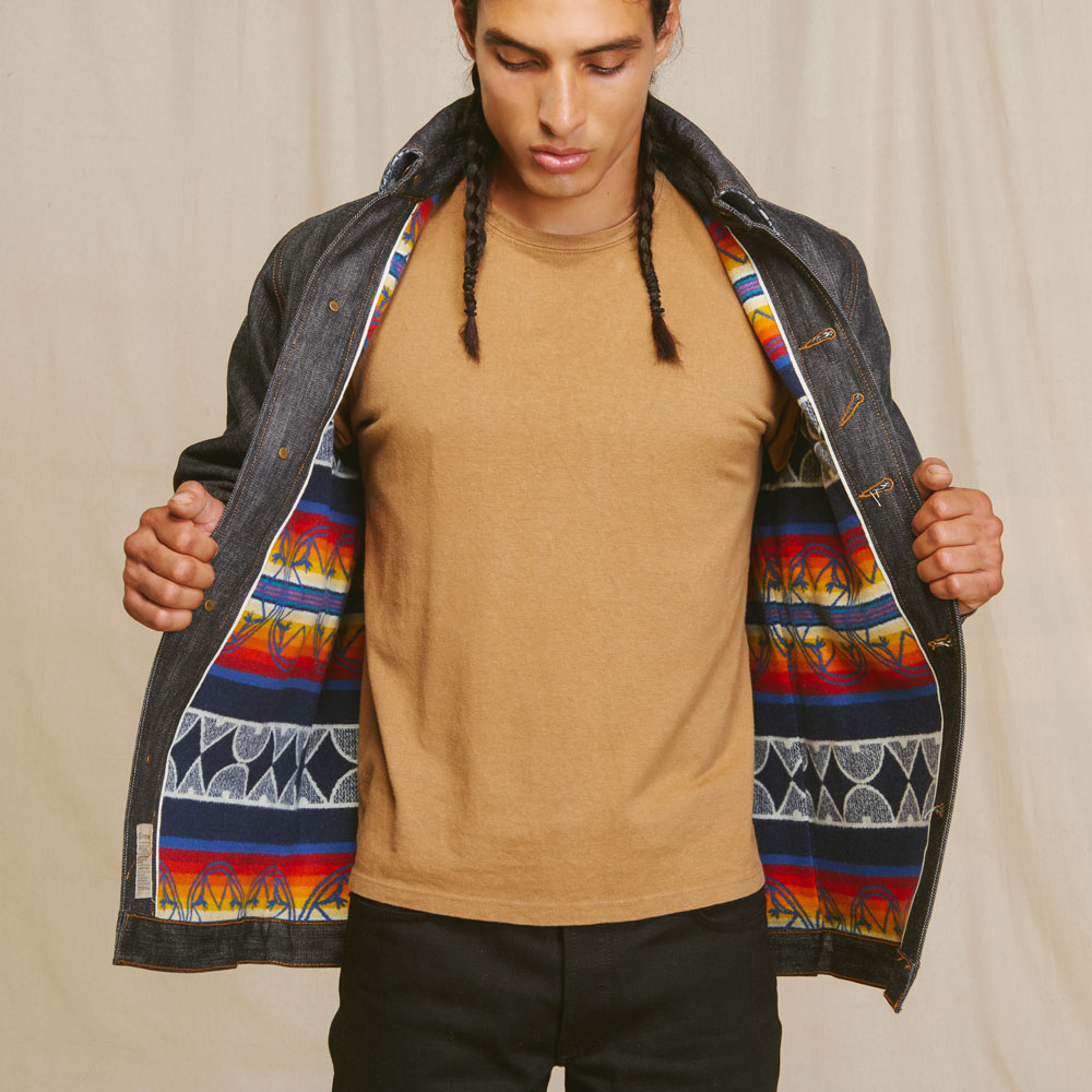 A Native American model stands facing the camera, with his denim Ginew jacket held open to show the Pendleton patterned wool lining.