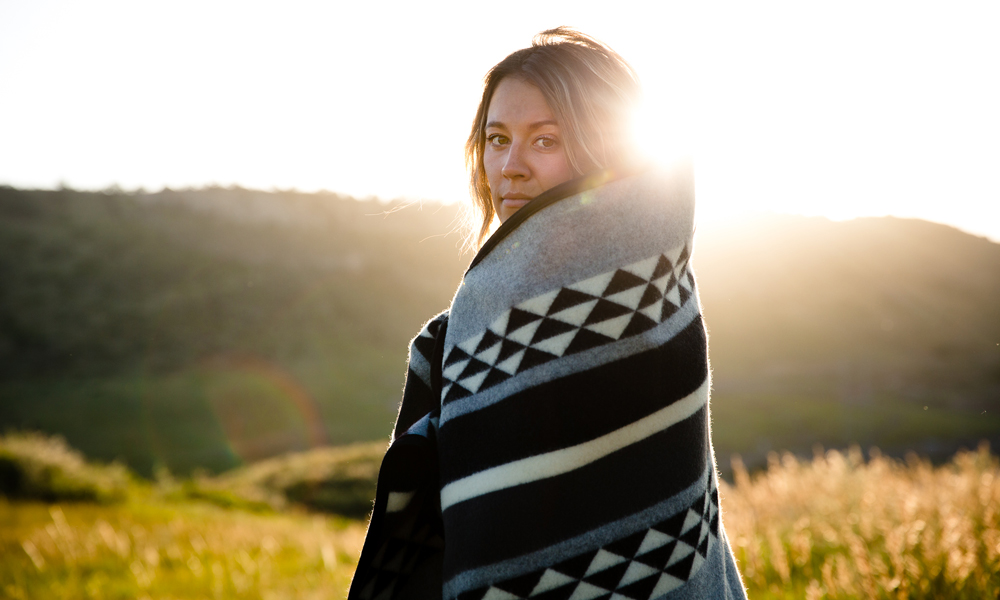 Kate_Rolston shot of a woman standing in a sunlit meadow, wrapped in a blanket.