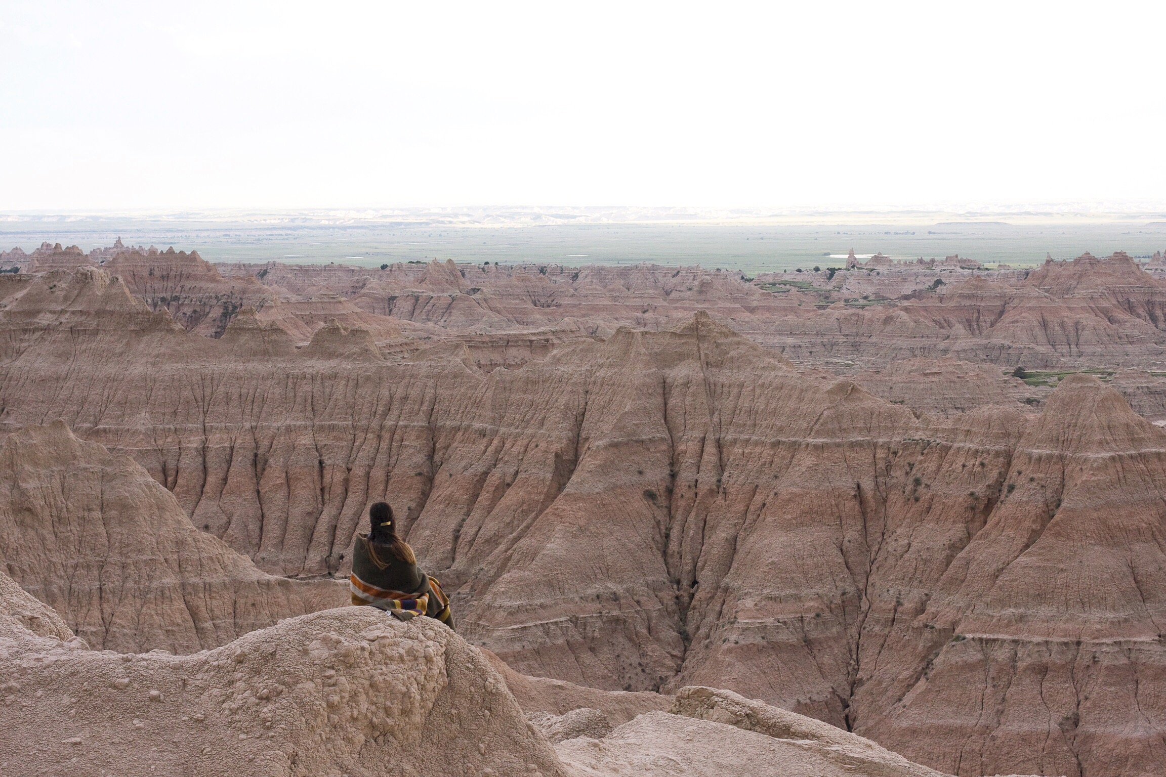 A woman wrapped in a Pendleton blanket looks at Badlands National Park - photo by emmanuel_beltran