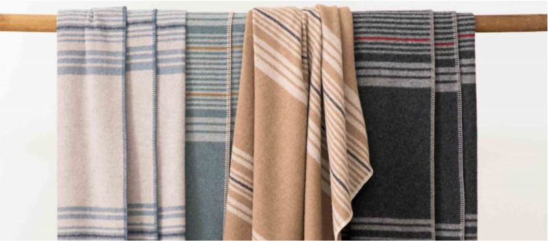 Four Pendleton Eco-Wise Wool striped throws draped across a wooden dowel.