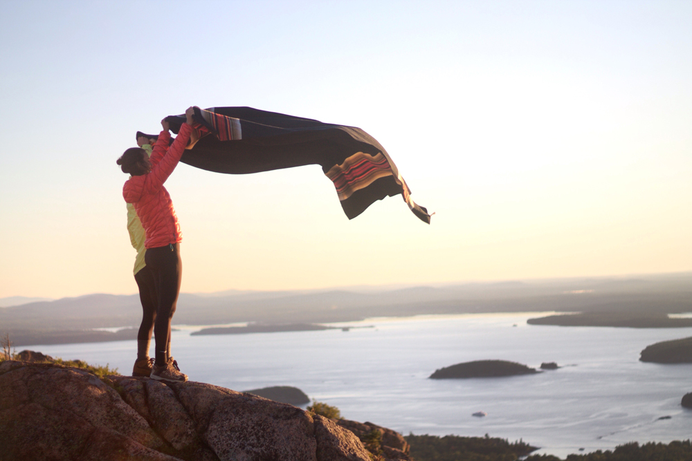 Karlov- A woman shakes out a blanket at the coastline of Acadia National Park.